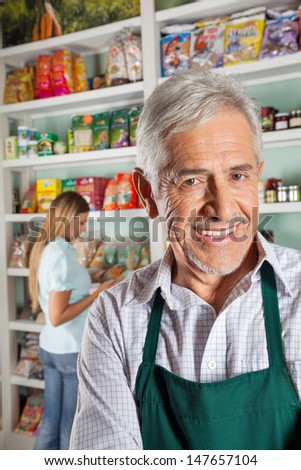 Portrait of happy senior male owner with female customer shopping in background