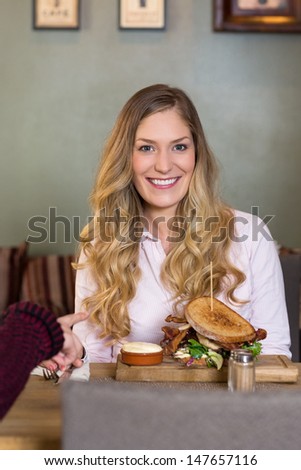 Portrait of young woman with burger at table in cafe