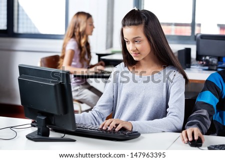 Teenage girl using computer at desk with friends in classroom