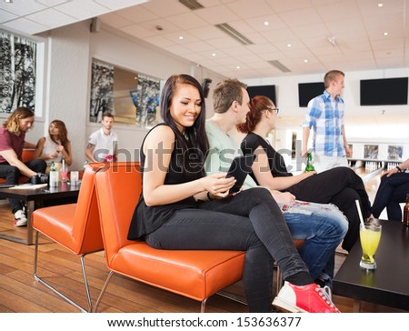 Beautiful young woman using digital tablet sitting with friends on couch in bowling club