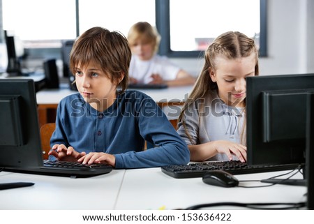 Cute little schoolchildren using desktop PC at desk in computer lab