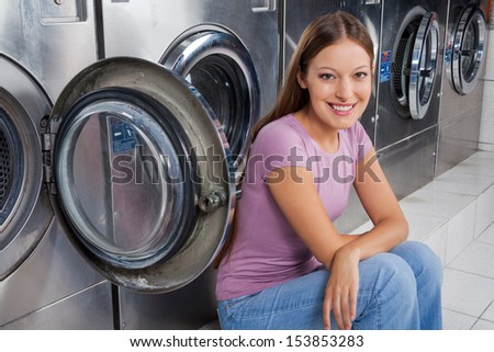 Portrait of beautiful young woman sitting against washing machines in laundry