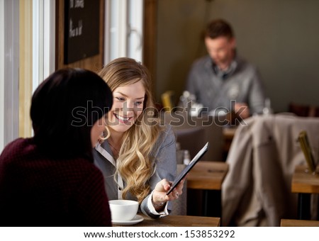 Two women sitting in rustic cafe looking at pictures on digital tablet
