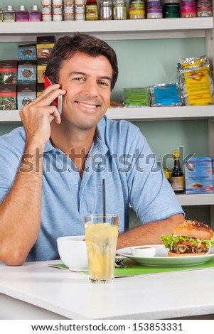 Portrait of happy mid adult man using cellphone with snacks at table in supermarket