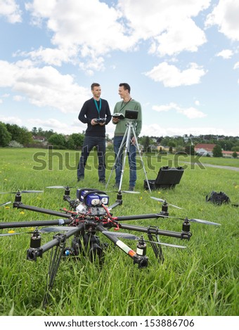 View of UAV helicopter on grass with technicians discussing in background at park