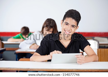 Portrait of male university student using digital tablet at desk in classroom