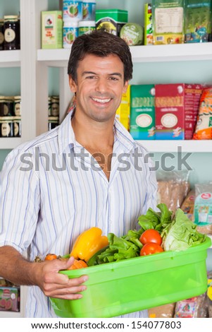 Portrait of happy mid adult man with vegetable basket in grocery store