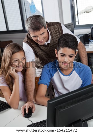 Mature male teacher with schoolchildren using computer at desk in lab