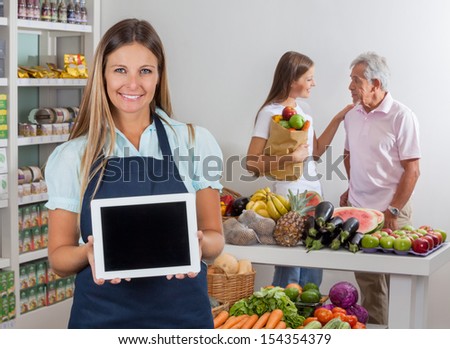 Portrait of saleswoman displaying digital tablet with father and daughter communicating in background