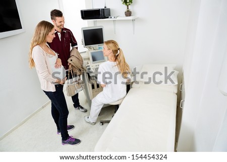 Female gynecologist using ultrasound machine while looking at expectant couple in clinic