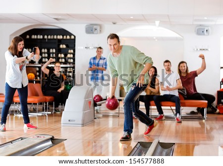 Young man bowling with friends cheering in background at club