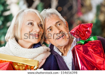 Happy senior couple with Christmas presents looking away in store