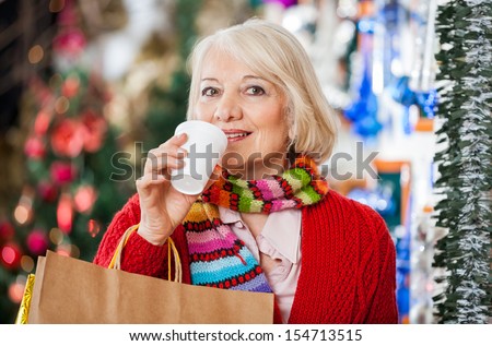 Portrait of beautiful senior woman with shopping bags drinking coffee at Christmas store
