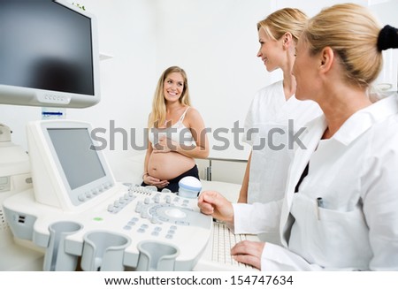 Gynecologists by ultrasound machine looking at pregnant woman in clinic