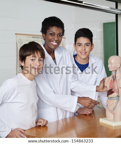 Portrait of young African American teacher pointing at anatomical model with students at desk in lab