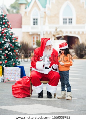 Full length of girl and Santa Claus with wish letter in courtyard