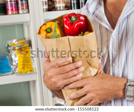 Midsection of male customer holding bag of fresh vegetables in grocery store