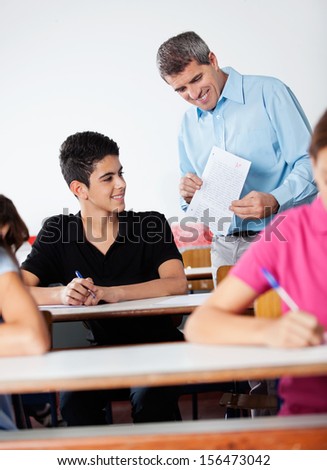 Mature male teacher and teenage schoolboy looking at paper during examination in classroom