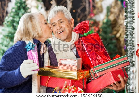 Senior woman kissing man holding stacked Christmas presents at store