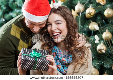 Cheerful young couple with present against Christmas tree in store
