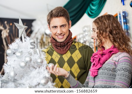 Portrait of happy young man shopping for Christmas tree with woman in store