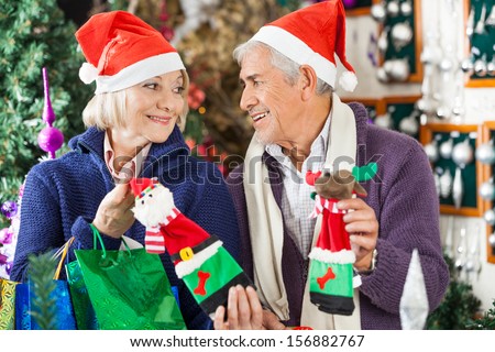 Senior couple in Santa hats looking at each other while shopping for Christmas decorations in store