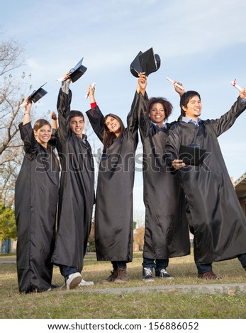 Full length of happy students with diplomas celebrating success on graduation day at college campus