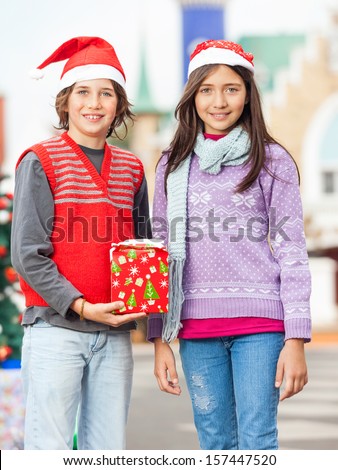 Portrait of smiling friends with Christmas gift in courtyard