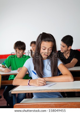 Female high school student writing paper at desk in examination