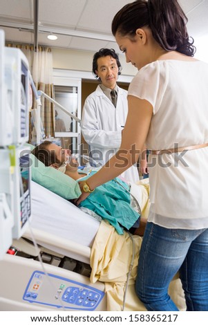 Doctor looking at woman standing by patient\'s bed in hospital room