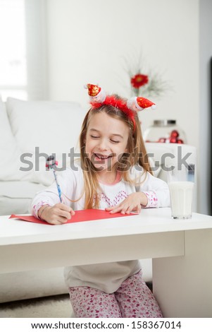 Happy cute girl writing letter to Santa Claus at home