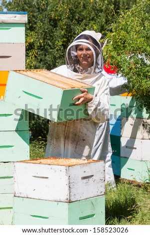 Portrait of beekeeper carrying honeycomb box while working at apiary