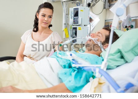 Beautiful woman looking at patient resting on bed in hospital