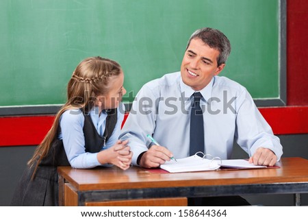 Mature male teacher looking at schoolgirl against chalkboard in classroom
