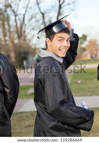 Portrait of happy male student in graduation gown holding certificate on university campus
