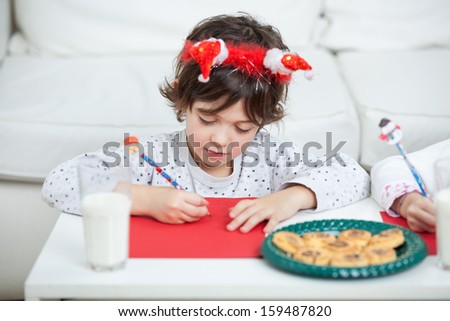 Cute boy with milk and biscuits writing letter to Santa Claus at home