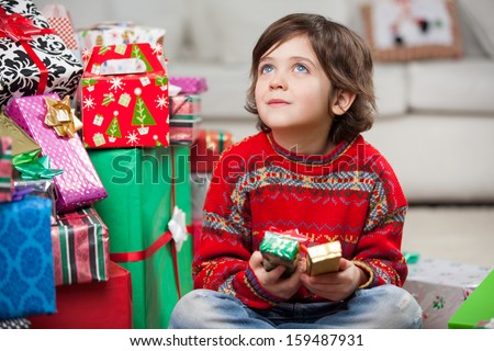 Thoughtful boy sitting by stacked Christmas gifts at home