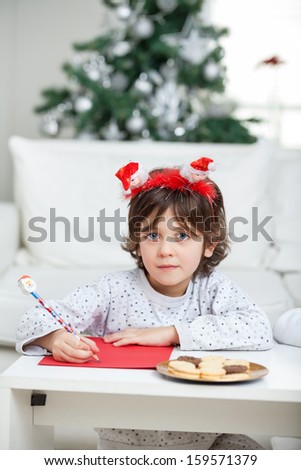 Portrait of boy wearing headband writing letter to Santa Claus at home