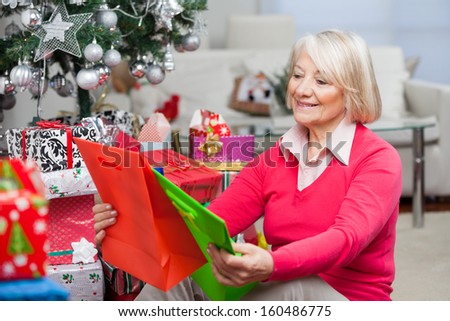 Smiling senior woman choosing bags while sitting by presents at home