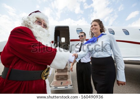 Airhostess and Pilot welcoming Santa against private jet at airport terminal