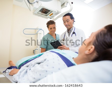 Medical team using digital tablet while young patient lying on xray table in examination room