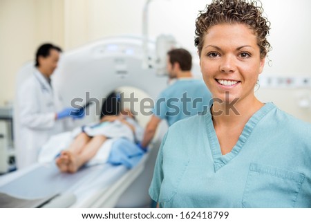 Portrait of happy female nurse with colleague and doctor preparing patient for CT scan in hospital