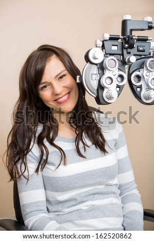 Portrait of beautiful young woman sitting behind phoropter during eye exam