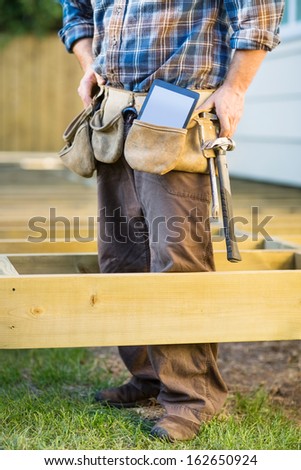 Low section of carpenter with tablet computer and hammer in tool belt
