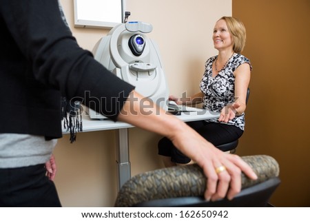 Happy mature female optician asking patient to sit in store