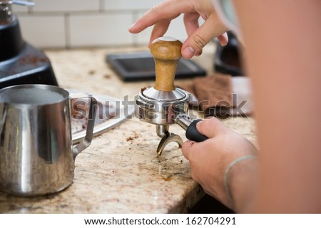 Cropped image of barista with portafilter and tamper in coffee shop