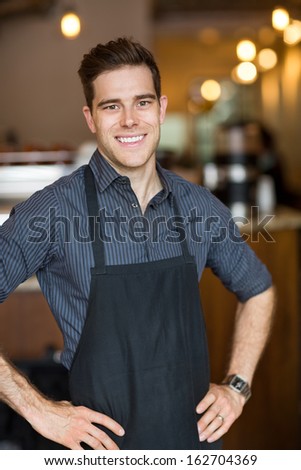 Portrait of happy male owner with hands on hips standing in cafe