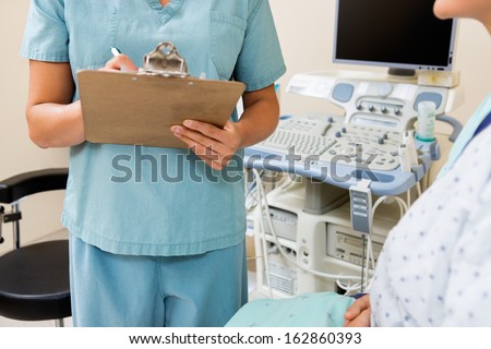 Midsection of female nurse writing on clipboard with patient in ultrasound room