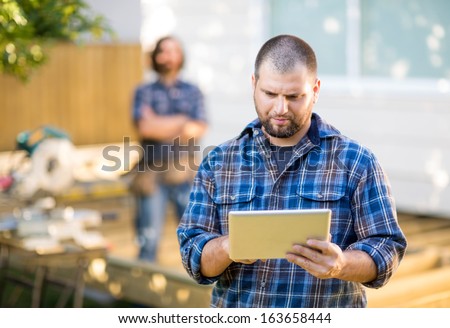 Mid adult manual worker using digital tablet with coworker standing in background at construction site