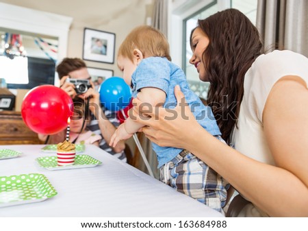 Father taking photo of mother and son in front of birthday cake at home